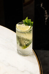 efreshing cocktail served in a tall glass with ice, lime wedges, and fresh mint leaves on a marble table. Perfect summer drink for bar, restaurant, or party concept © Влад Пентюк