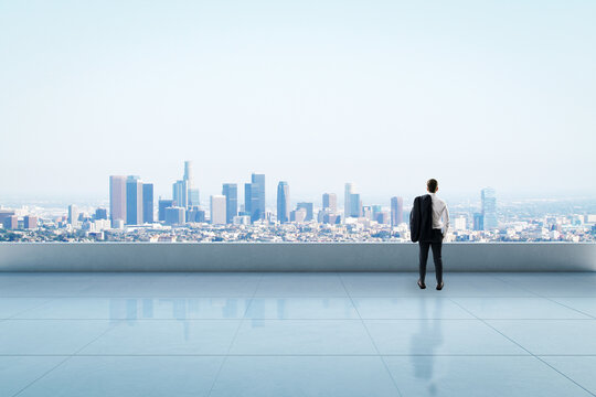 Businessman standing on rooftop looking at city skyline in daylight, concept of future vision, planning, and urban development in business.