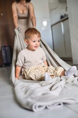 Fototapeta premium Happy child spending time at home while mother playfully pulls him on a blanket across the floor
