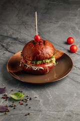uicy gourmet burger with a fresh tomato slice on top of the bun. Delicious beef patty, melted cheese, lettuce, and vegetables served in a rustic bread bun. Appetizing fast food meal, perfect for lunch