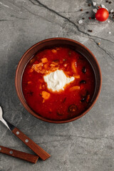 Traditional Russian-Ukrainian soup solyanka served with sour cream and fresh herbs. Rich, hearty broth with smoked meat, pickles, olives, lemon slice, and flavorful spices. Close-up of hot homemade di