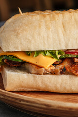 Tasty sandwich in a golden toasted bun with juicy meat and fresh vegetables. Close-up of delicious fast food snack filled with grilled beef, lettuce, tomato, cucumber, and melted cheese. Appetizing st
