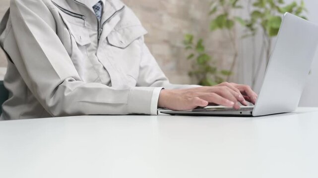 作業服を着てパソコン作業をする男性の手元