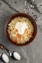 Close-up of hot homemade chicken broth with noodles, carrot, and fresh herbs served in a rustic ceramic bowl. Traditional comforting soup of Ukrainian and Eastern European cuisine. Nutritious and auth