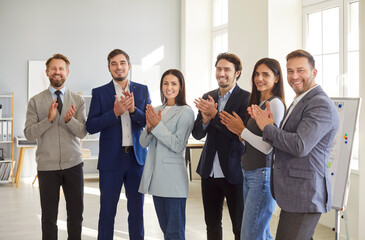 Group portrait of successful business professionals in office environment clapping, expressing support and recognition. Smiling colleagues creating atmosphere of trust, success and corporate unity.