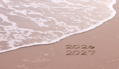 Handwritten inscription 2026 and 2027 on the beach in the sunset time. The concept of Goodbye 2026 and Happy New Year 2027