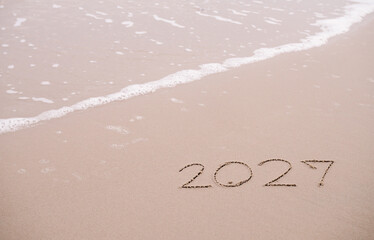 2027 year handwritten on the beach in the sunset time. New Year 2027 concept