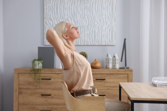 Mature woman stretching on chair in office - Powered by Adobe