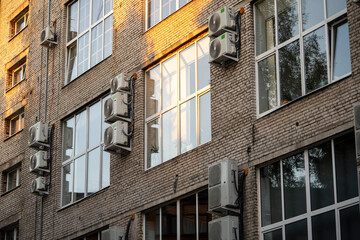 Facade of building with many air conditioners on windows in southern hot country. Yellow house exterior on city street. Escape from heat, creating favorable microclimate in urban apartments concept.