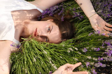 Beautiful young woman lying among lavender flowers outdoors, closeup