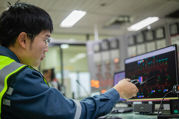 Technician Monitoring Power Grid Data on Computer Screen in Control Room with High-Visibility Safety Vest