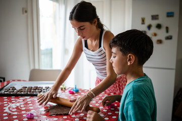 Sister and brother flattening dough with rolling pin, baking cookies at home