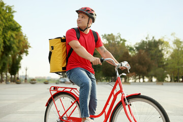 Courier with thermo bag riding bicycle outdoors. Food delivery service