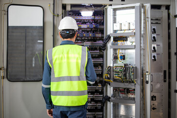 Electrical technician inspecting control panel with safety gear in industrial setting with bright lighting