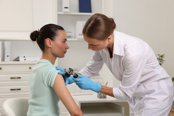 Fototapeta premium Doctor examining young woman's mole with dermatoscope in hospital