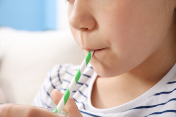 Little girl drinking refreshing drink through straw at home, closeup