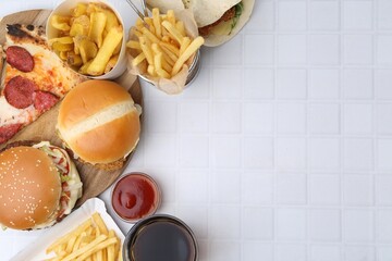 Different delicious fast food, ketchup and cola on white tiled table, flat lay. Space for text