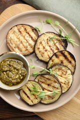 Grilled slices of eggplant with sauce and microgreens on wooden table, top view