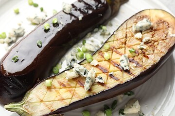 Slices of grilled eggplant with green onion and blue cheese on table, closeup
