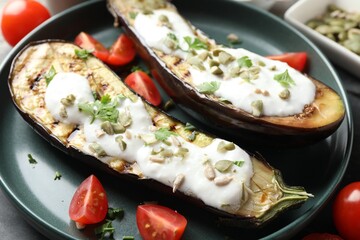 Slices of grilled eggplant with pumpkin seeds, tomatoes and yoghurt on table, closeup