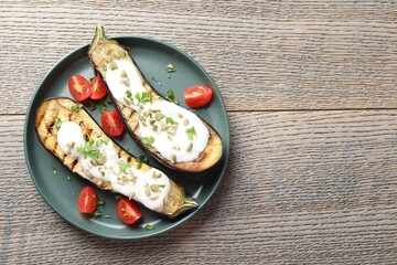 Slices of grilled eggplant with pumpkin seeds, tomatoes and yoghurt on wooden table, top view. Space for text