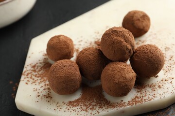 Tasty chocolate candies with cocoa powder on black table, closeup