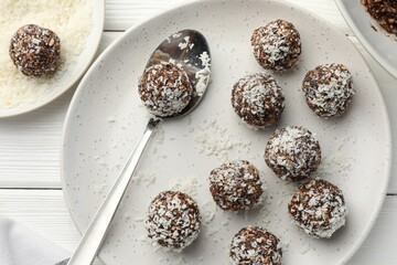 Tasty chocolate candies with nuts and coconut flakes on white wooden table, flat lay