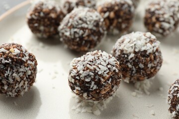 Tasty chocolate candies with nuts and coconut flakes on plate, closeup