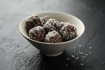 Tasty chocolate candies with nuts and coconut flakes in bowl on black table, closeup