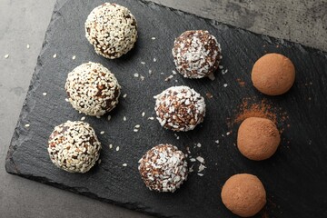 Tasty chocolate candies with cocoa powder, nuts, coconut flakes and sesame seeds on grey table, top view
