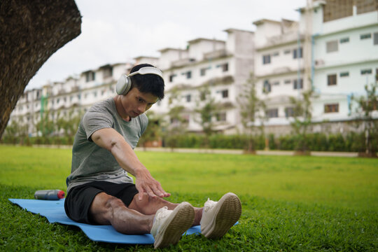 Young man stretching his legs on yoga mat outdoors while exercising in a green park. Healthy lifestyle concept.