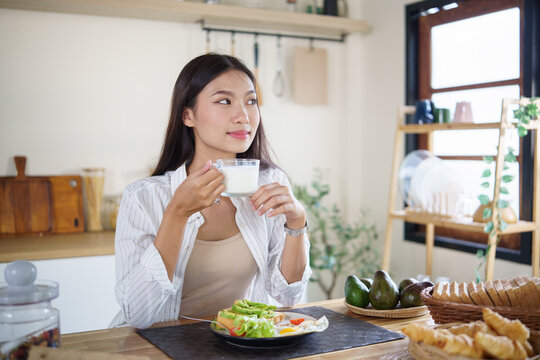 Young woman enjoying a glass of milk while having a healthy breakfast at home. Healthy lifestyle concept.