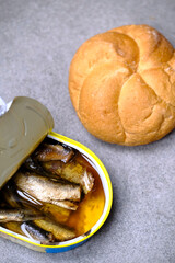Bun and sprats in tin can on grey textured table, top view
