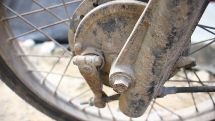 Closeup of a rusty, weathered motorcycle rear wheel hub and brake system, showcasing aged metal, dirt, and rugged use in an outdoor environment