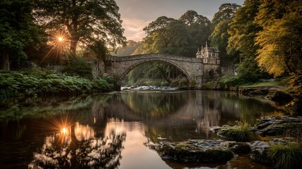 Fototapeta premium A serene stone bridge reflects in the still waters of a river at dawn, bathed in golden sunlight.