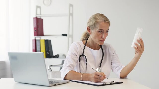 Female doctor in white medical uniform examines a jar and takes notes in a bright office. Concept medical diagnostics.