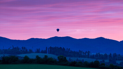 A solitary hot air balloon drifts gently across a twilight sky, framed by majestic, shadowy mountain silhouettes below.