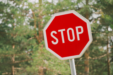 Red stop sign standing before blurred green trees, representing traffic regulations and safety