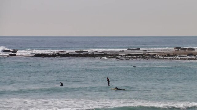 Surfers ride waves at Los Ca&ntilde;os de Meca beach near the Trafalgar lighthouse on the C&aacute;diz coast, Andalusia, Spain. A vibrant scene of sport, nature, and coastal energy.