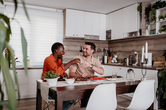 Two friends enjoy a meal together in a modern kitchen while sharing drinks and laughter