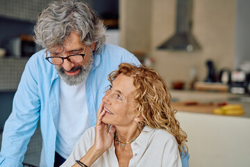 Cheerful senior couple using laptop, browsing internet and smiling while relaxing in kitchen at home