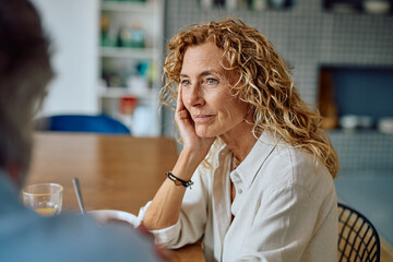 Thoughtful mature woman listening during a serious conversation with her partner at the kitchen table