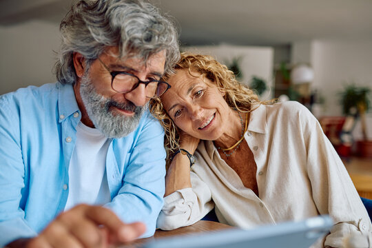 Smiling senior couple using digital tablet at home, enjoying modern technology and online communication - Powered by Adobe