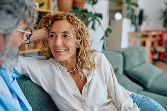 Senior couple enjoying each other's company, chatting and smiling while relaxing on the sofa in their cozy living room
