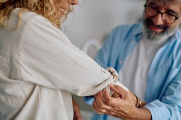 Mature man rolling up the sleeve of a mature woman's shirt, sharing a tender moment in their cozy kitchen, embodying love and support
