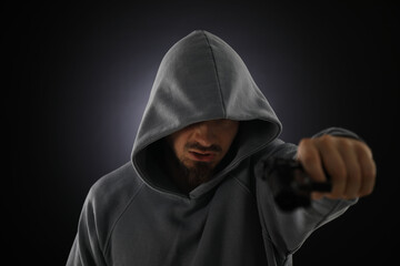 Criminal with gun on dark background, selective focus