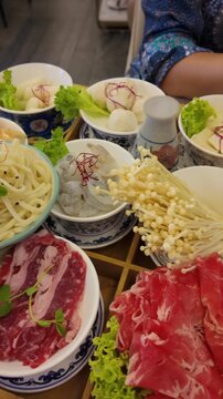 Asian restaurant menu on the tabel featuring hot pot broths, ramen, seafood, meats, vegetables, and tofu.