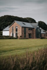 Obraz premium Modern brick house with large windows situated in a scenic green landscape during the daytime in a tranquil countryside setting