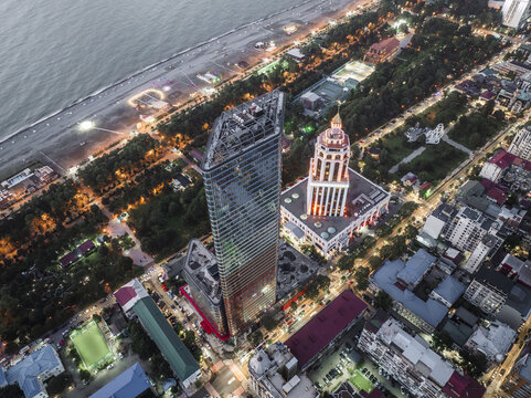 Aerial view of illuminated skyscrapers and the Radisson Blu Hotel sparkle against the dark sea and cityscape, a vibrant contrast of light and shadow, Batumi, Adjara, Georgia.