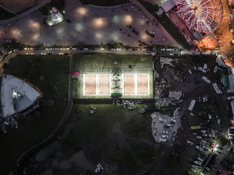 Aerial view of illuminated tennis courts casting a bright glow amid the surrounding darkness, with the Ferris wheel adding a colorful splash of light, Batumi, Adjara, Georgia. - Powered by Adobe